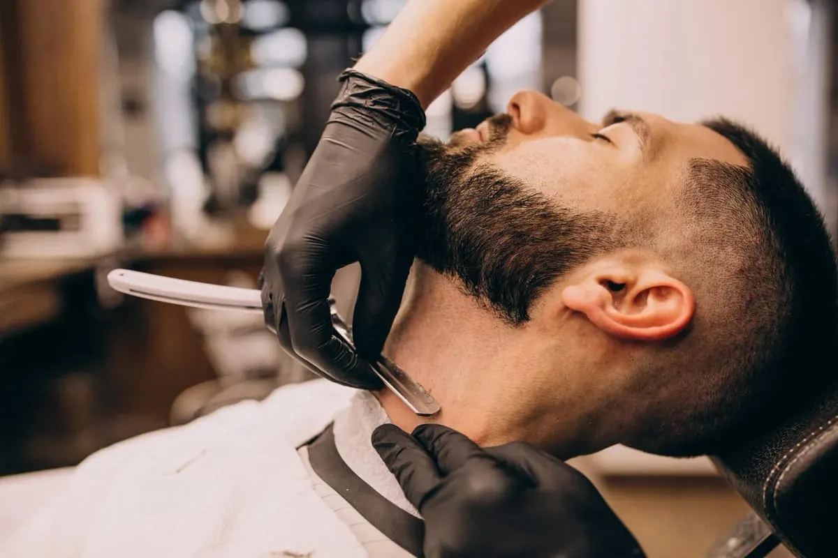 A barber trimming a beard with a razor