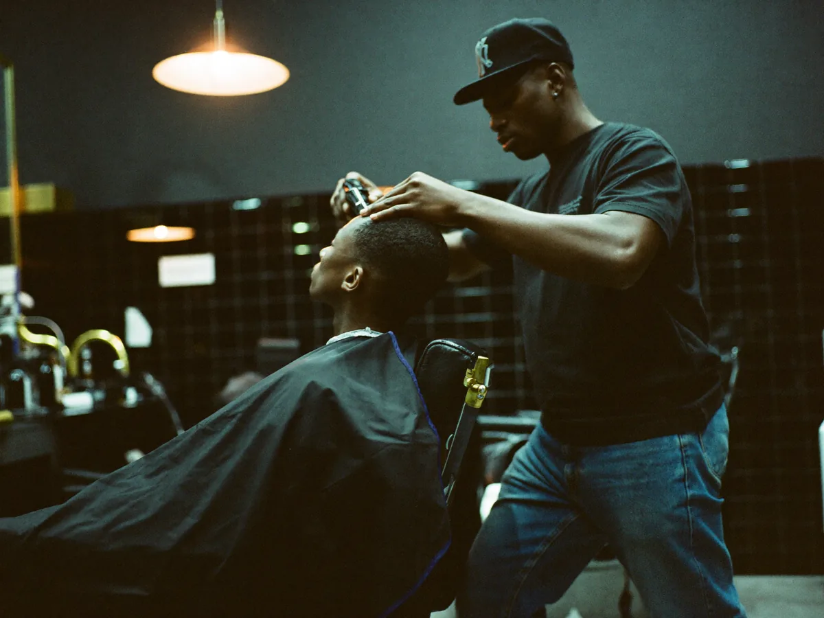 A barber cuts a client's hair in a dark barbershop with teal tiles | Buiiild.com