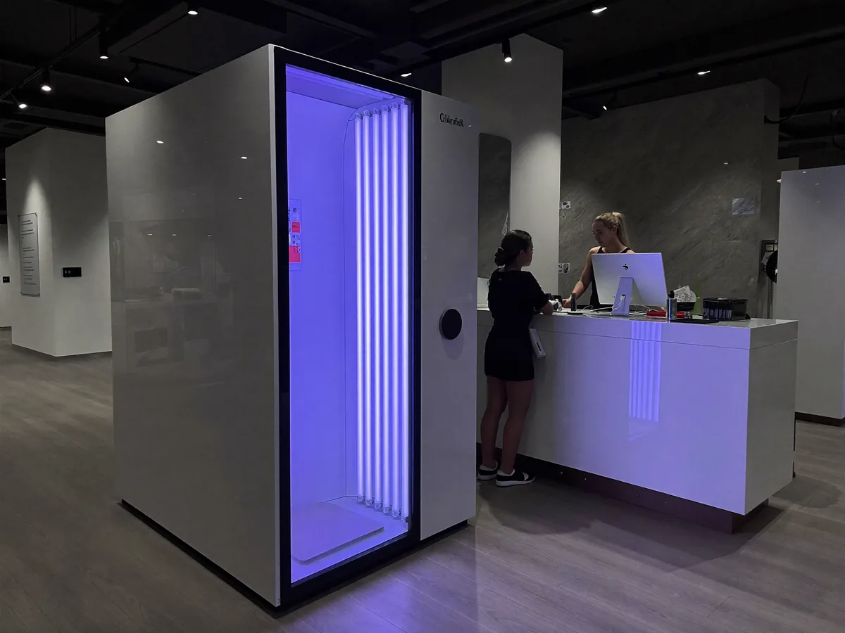 The reception of a modern tanning salon, with a sunbed glowing in violet light | Buiiild.com