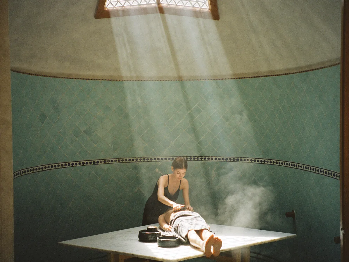 A scrub on the marble slab of a hammam with turquoise tiles, in steam and soft light | Buiiild.com