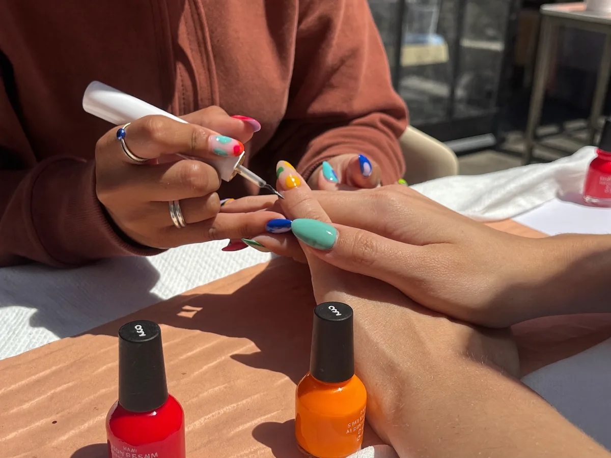 A nail technician paints colourful nail art on a client's nails | Buiiild.com