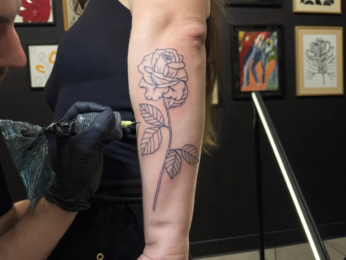 A gloved tattoo artist draws a fine-line rose on a client's forearm | Buiiild.com